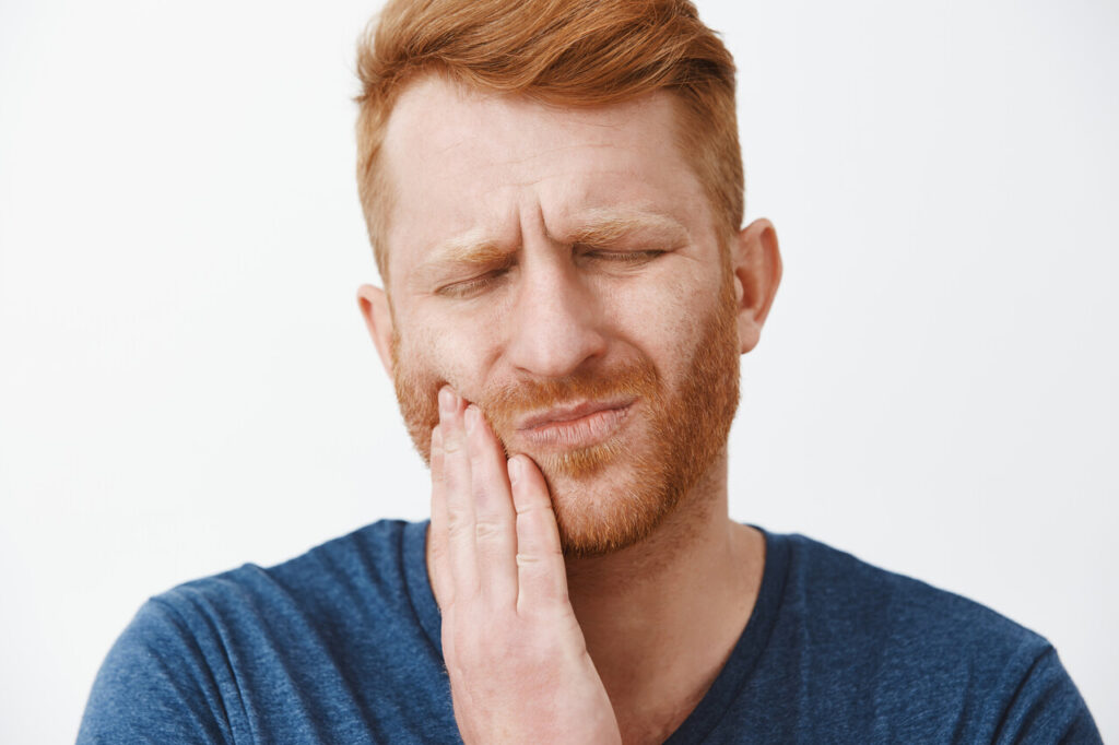 homem ruivo com dor no dente simbolizando uma inflamação no dente.