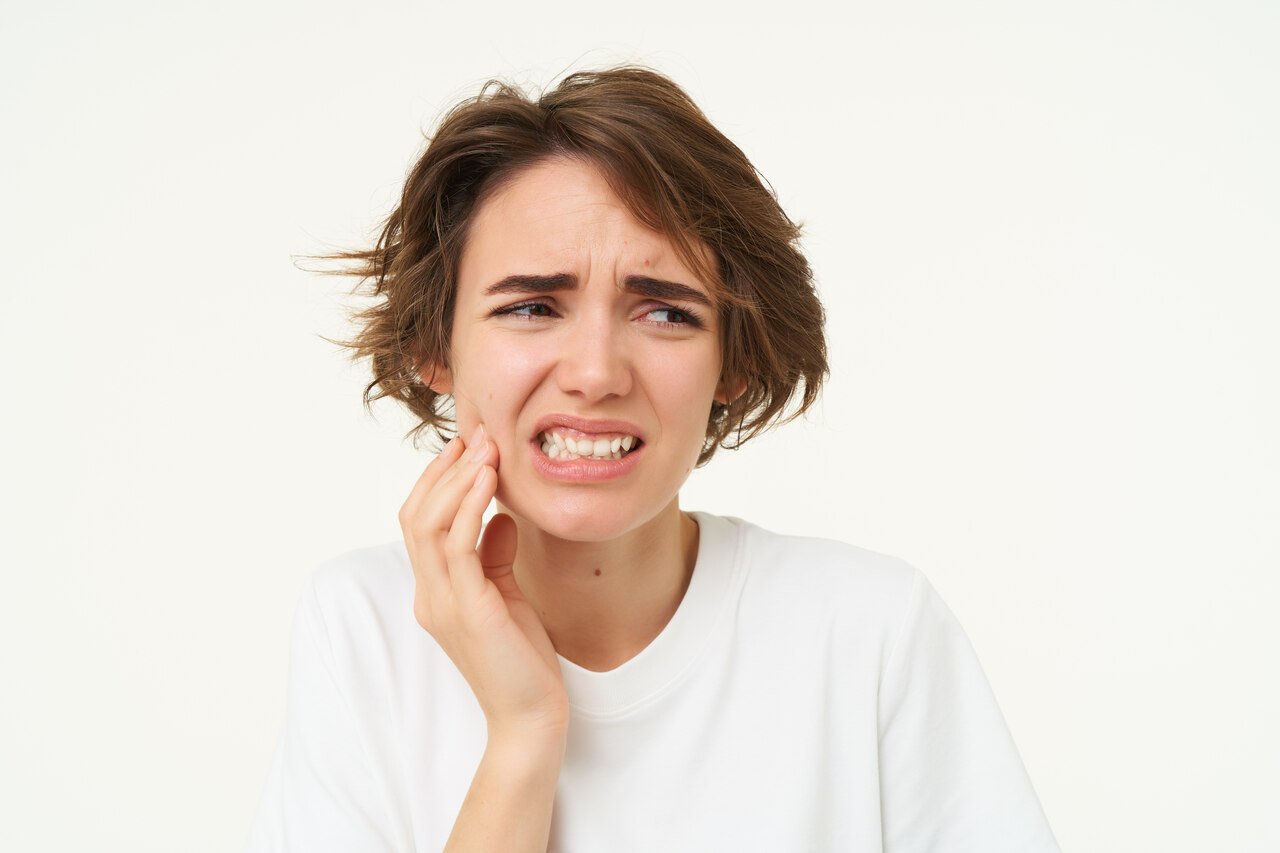 Mulher com cabelo curto e blusa branca se queixando de dor de dente por conta de cáries recorrentes.